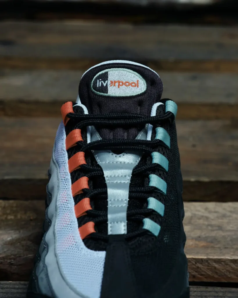 Close-up of a black and white sneaker with orange and teal lace loops and a Liverpool tongue logo on wooden planks