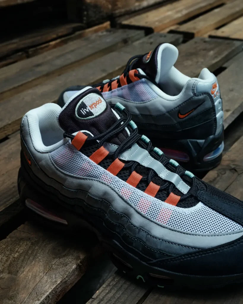 Pair of grey and black Nike Air Max 110 sneakers with orange accents on a weathered wooden surface
