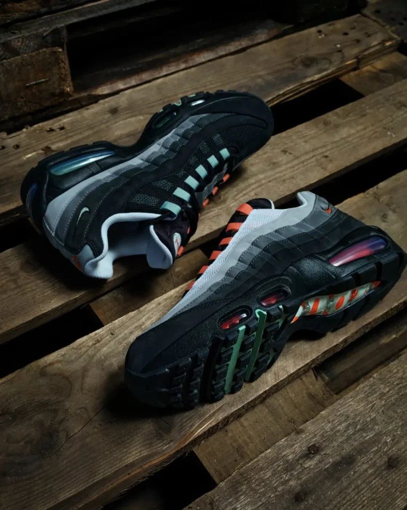 Pair of black and gray Nike Air Max 95 sneakers with orange and green accents on a weathered wooden pallet