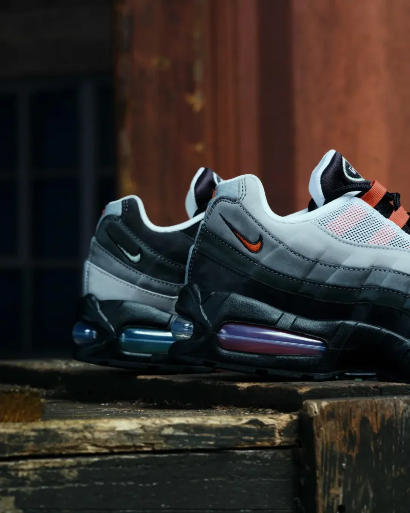 Pair of black, gray and white Nike shoe with orange accents and visible air cushions on a weathered wooden surface
