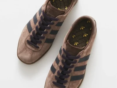 Pair of brown suede adidas sneakers with black stripes and dark laces on a white background