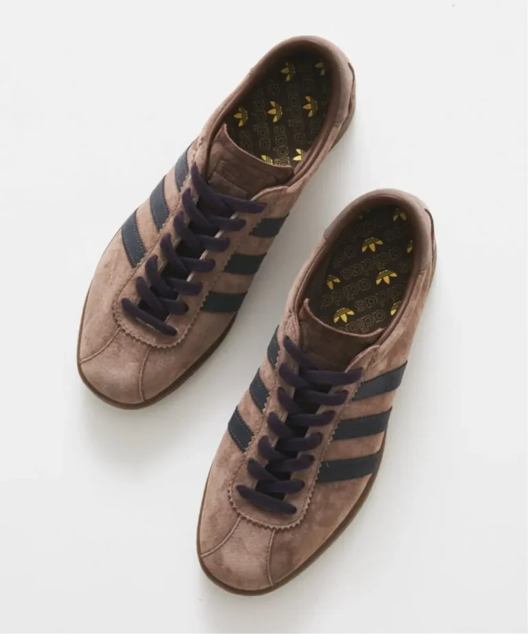 Pair of brown suede adidas sneakers with black stripes and dark laces on a white background