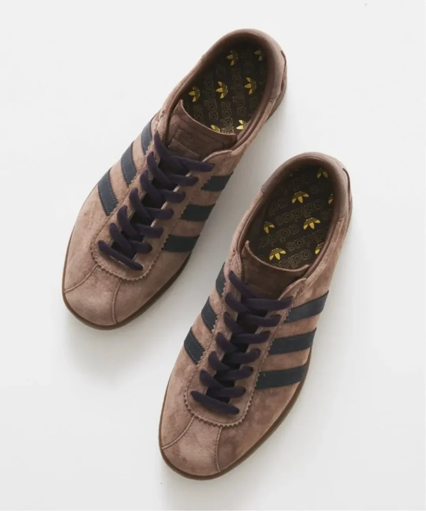 Pair of brown suede adidas sneakers with black stripes and dark laces on a white background