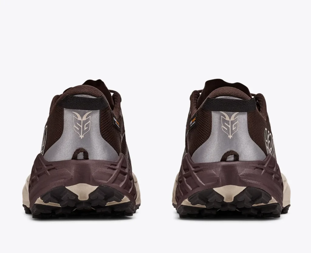 Pair of brown trail run shoe shown from the rear, with silver heel panels, cream midsoles and black lugged outsoles on