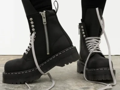 Black platform boots with silver zippers, white laces, and deep lugged soles worn over black leggings on a concrete floor