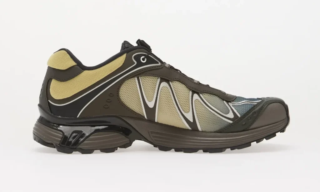 Side-view trail shoe in brown, black, beige, and gray mesh with white wavy overlays and rugged lugged sole on a white