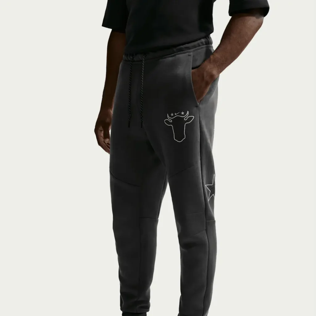 Cropped model wearing black joggers with a white cow-head emblem and star graphic on the leg against a light background