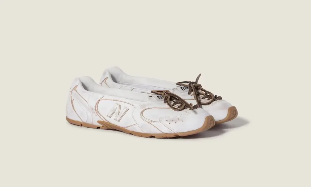 Pair of white New Balance sneakers with brown laces and gum soles on a beige background