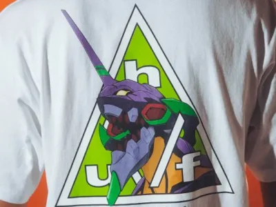 Back of a white T-shirt featuring a colorful Evangelion character graphic inside a triangular logo, against an orange