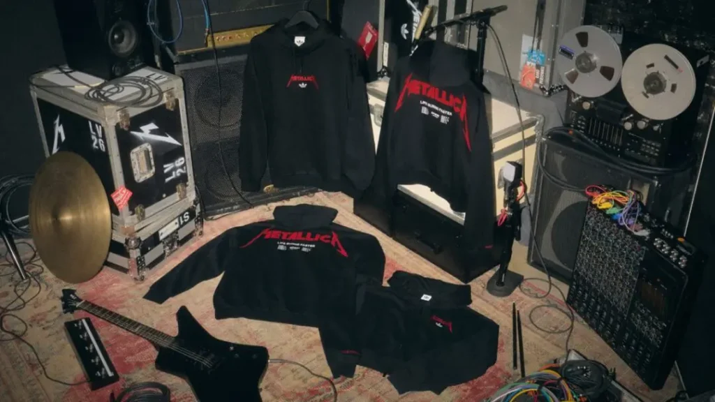 Black Metallica-branded hoodies and shirts displayed among stage equipment, a guitar, cables, and reel-to-reel audio gear