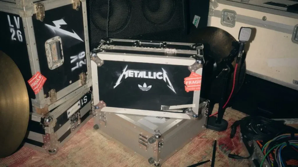 Metallica-branded black and silver equipment cases with red fragile tags sit among cables and a cymbal backstage
