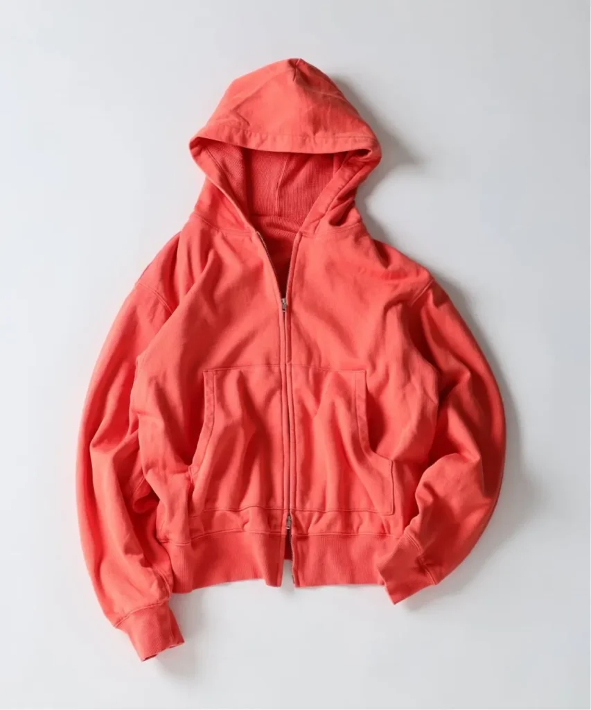 Coral-red zip-up hoodie with a drawstring hood and large front pouch pocket, laid flat on a white background