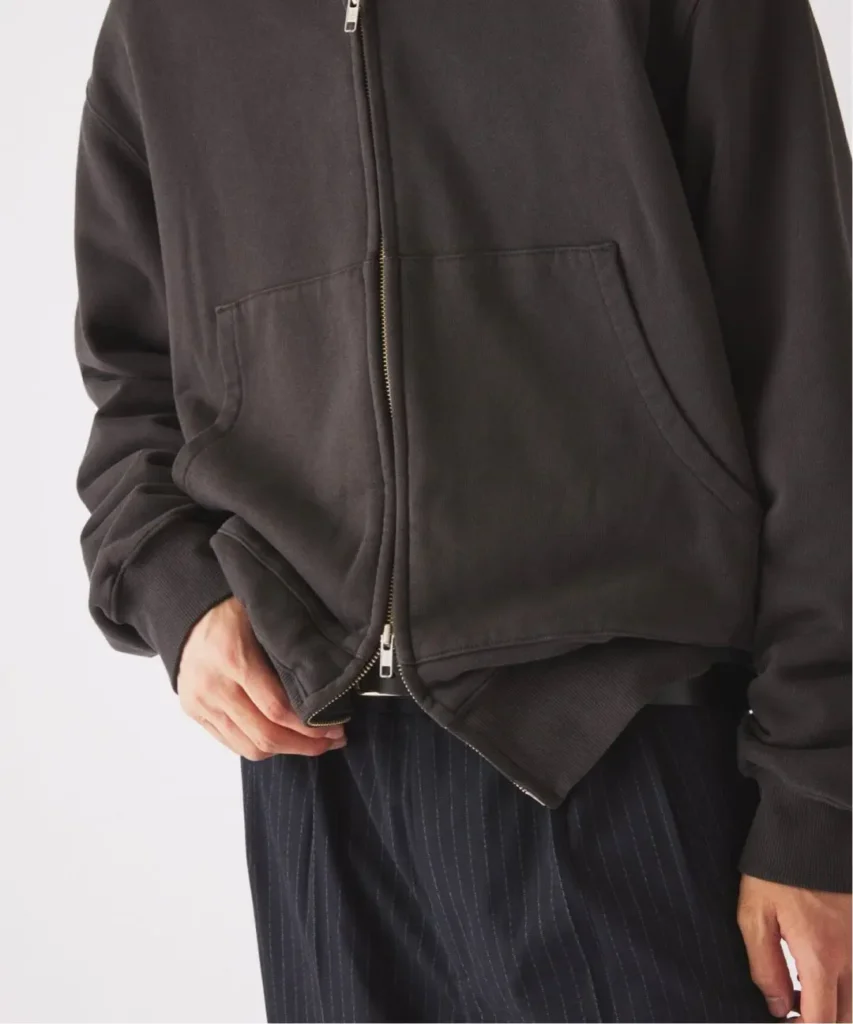 Cropped model wearing a charcoal zip-up hoodie with front pockets and ribbed cuffs over dark pinstriped trousers