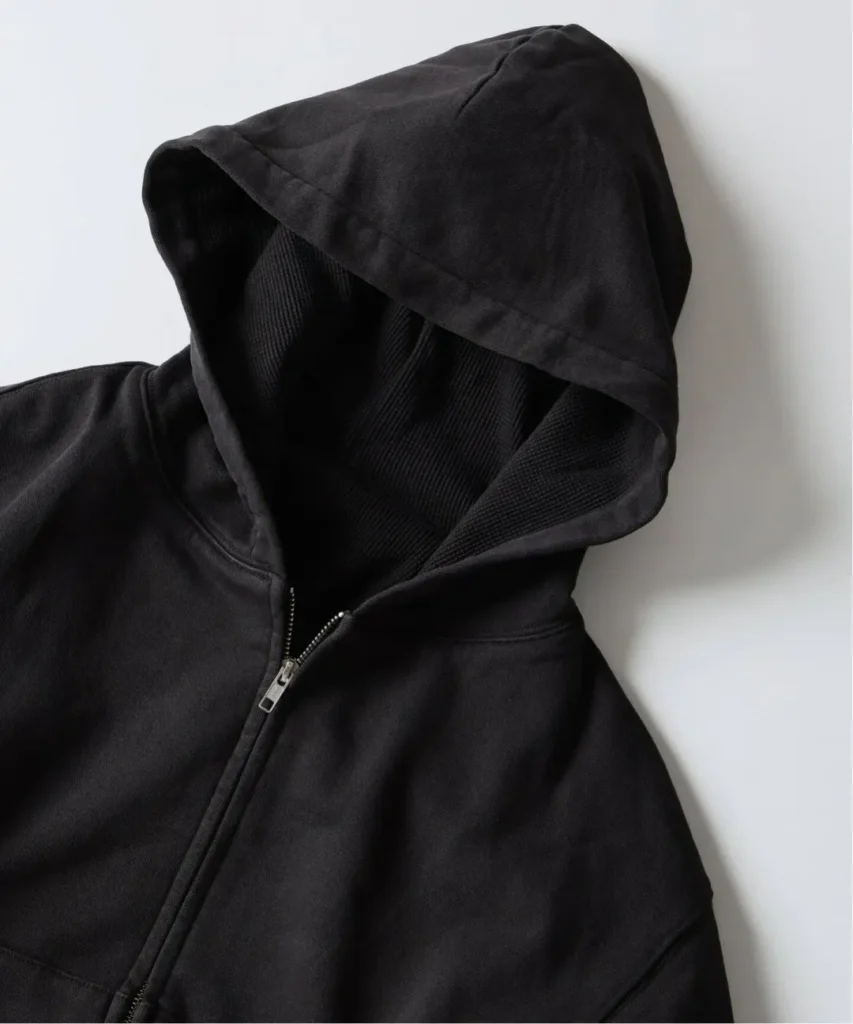 Close-up of a black zip-front hoodie with an oversized hood and textured double-face lining against a white background