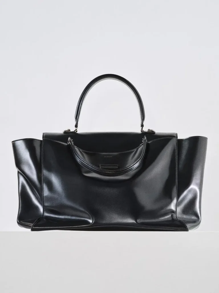 Black leather tote bag with twin handles and folded side panels on a white background