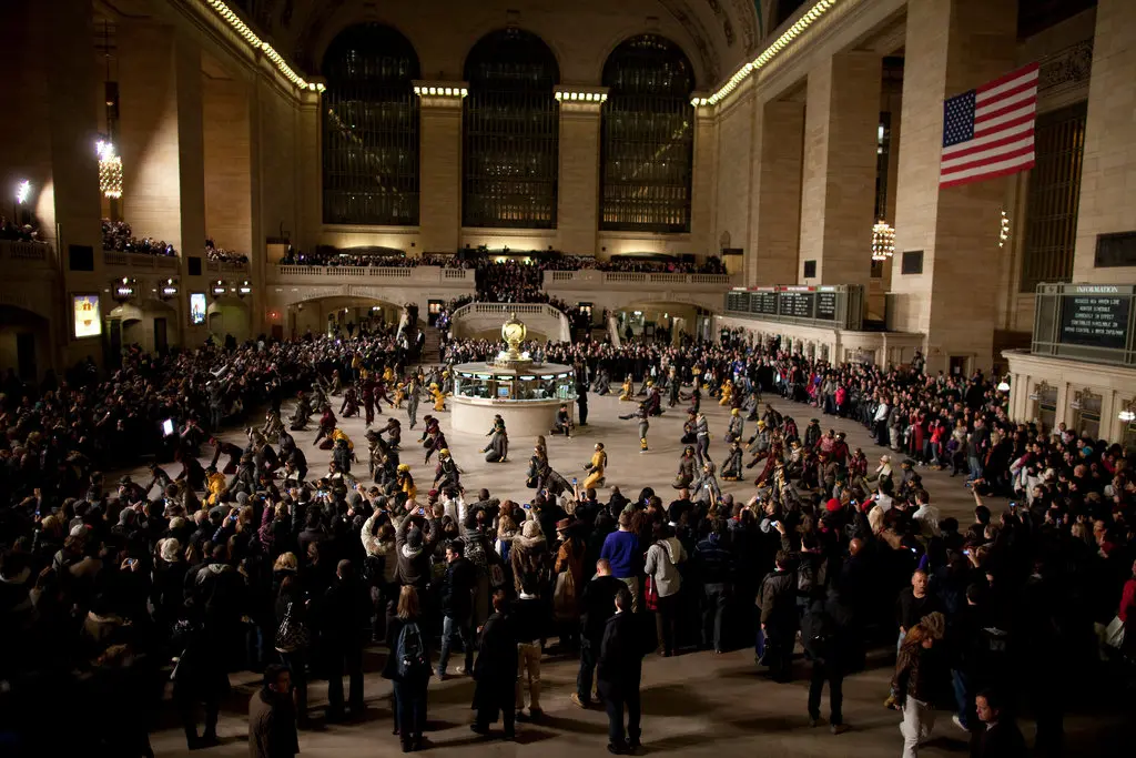 Crowd gathers around dancers in New York's Grand Central Terminal beneath a large American flag