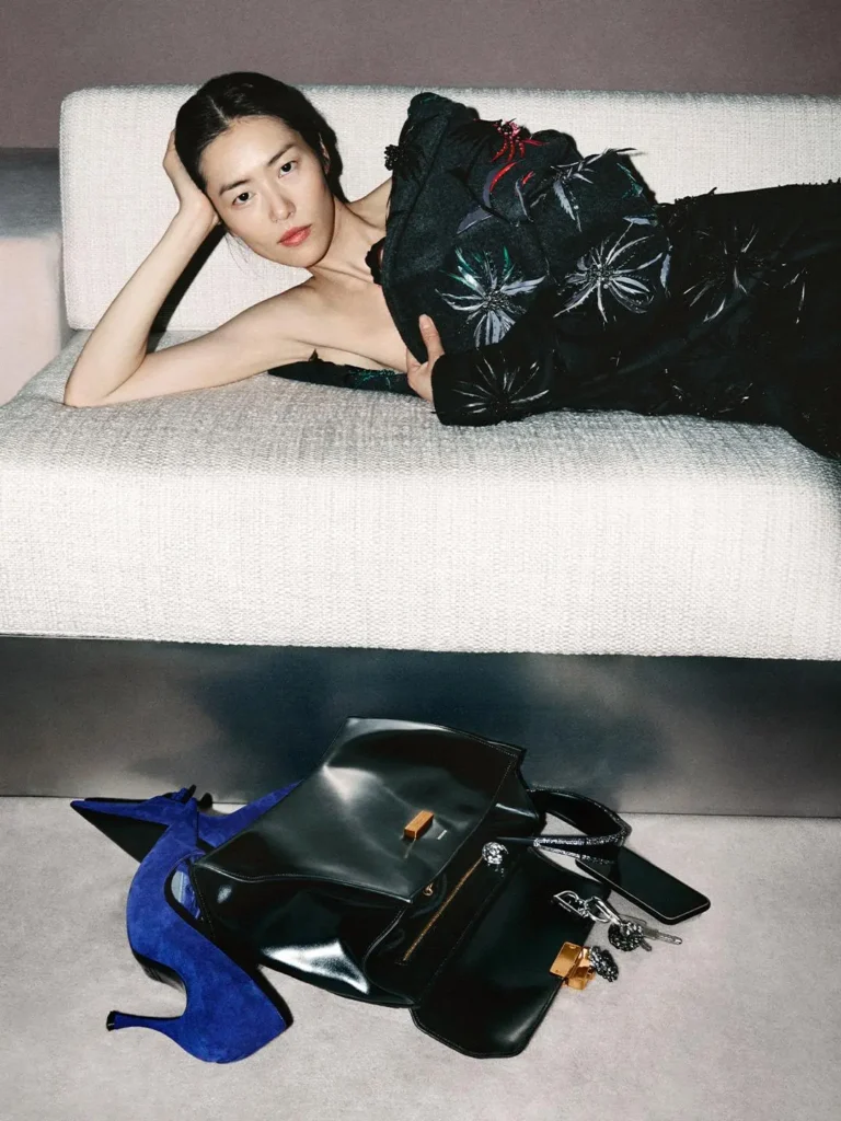 Person reclining on a white sofa in a black floral dress, with black handbags and blue heels on the floor below