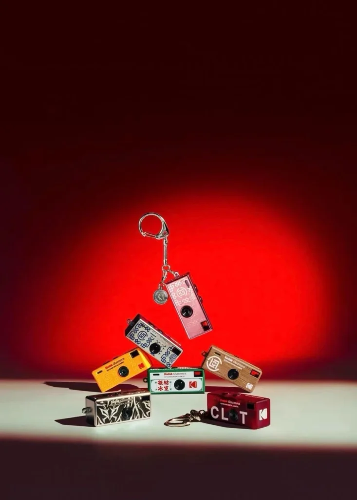 Several colorful Kodak Charmera miniature cameras and keychains arranged on a surface against a red background