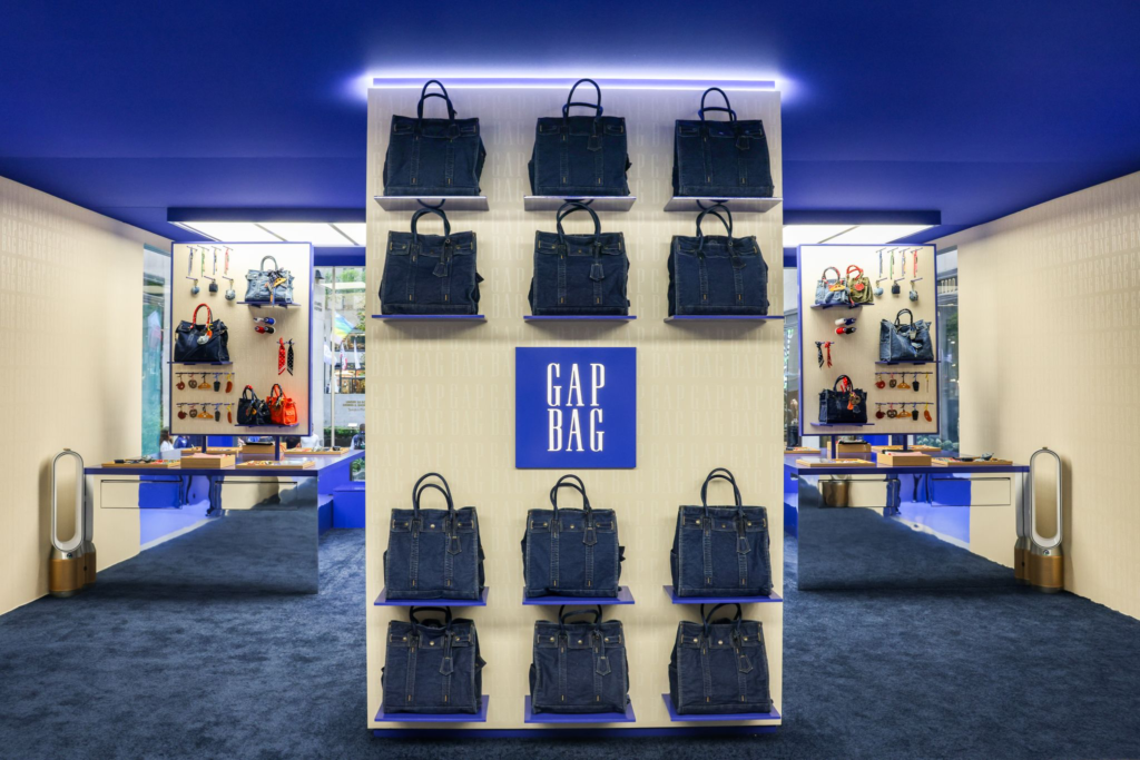 Display wall lined with dark denim handbags and a central blue GAP BAG sign in a brightly lit showroom