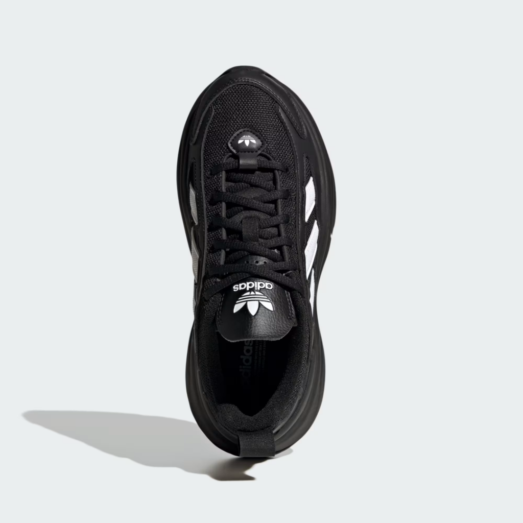 Top-down view of a black Adidas shoe with white stripes, black laces, and a thick sole on a pale background