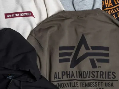Alpha Industries sweatshirts and jacket arranged together, featuring maroon logo patches and large printed branding in gray