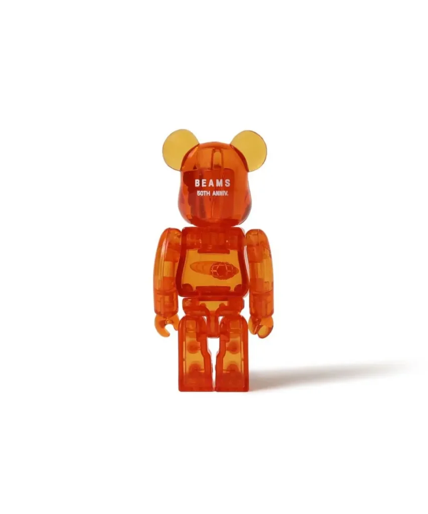 Translucent orange BE@RBRICK figure with yellow ears, BEAMS 50TH ANNIV. text, and a chest graphic on white background