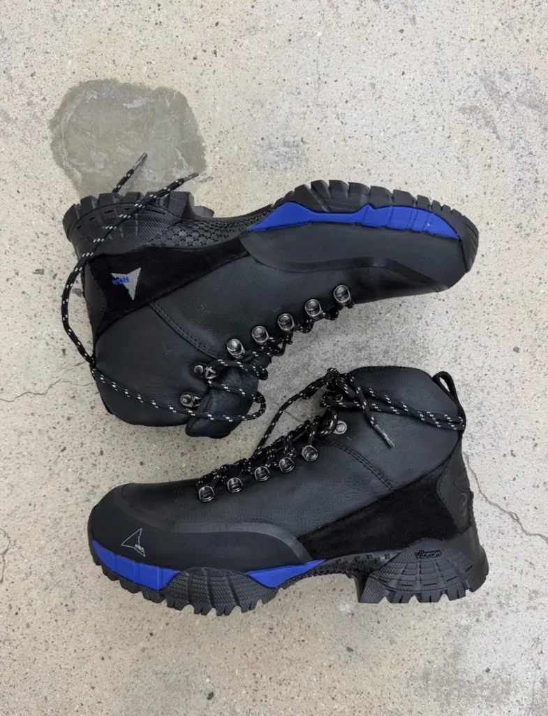 Two black hiking boots with blue accents, rugged soles and black laces on a concrete surface