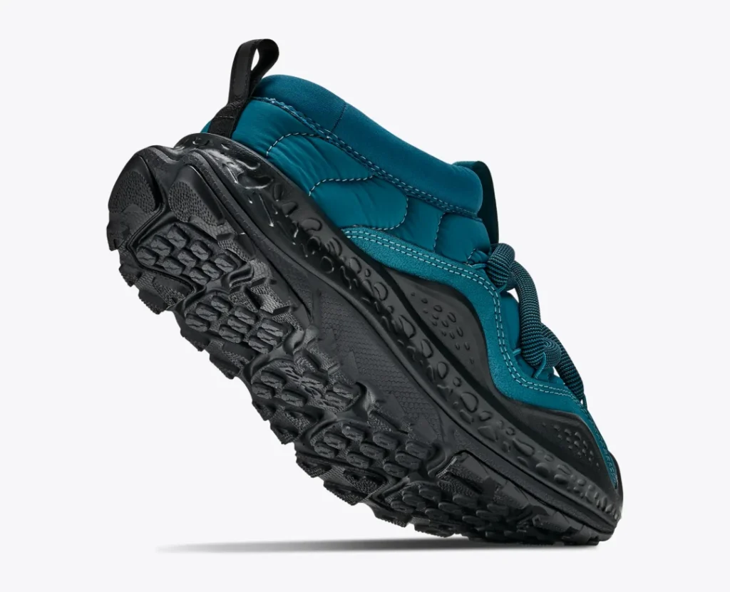 Teal quilt Hoka slip-on shoe with black rugged treaded sole, tilted diagonally against a white background