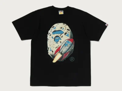 Black Tee laid flat on a pale background, with an illustrated moon and red-and-blue rocket graphic on the chest