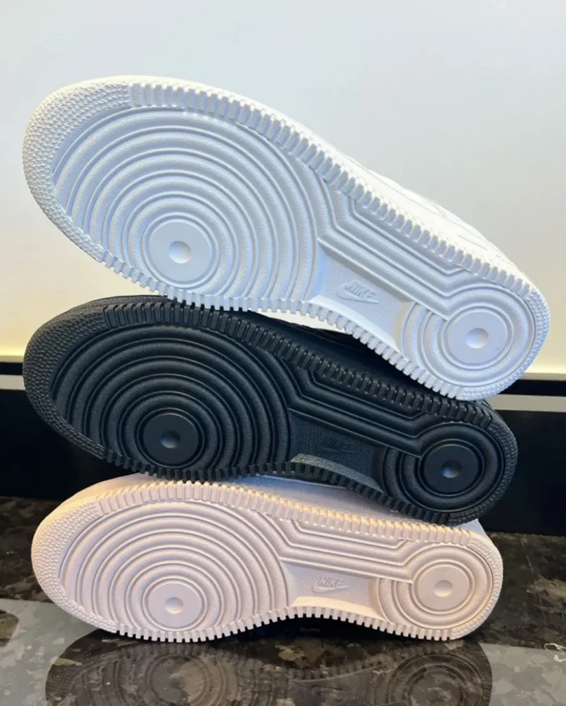 Three Nike sneaker soles stacked diagonally: white on top, black in the middle, and off-white at the bottom
