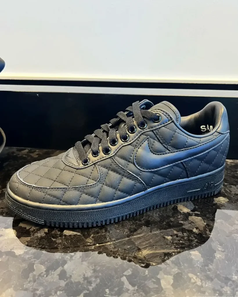 Black quilted Nike low-top sneaker with black laces and swoosh on a dark marble countertop