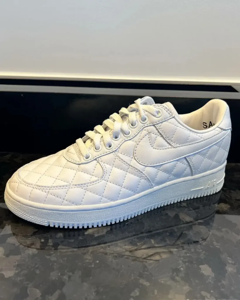 White quilted low-top sneaker with laces and swoosh logo, displayed on a dark reflective surface