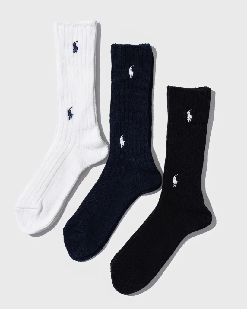 Three ribbed crew socks in white, navy, and black, each featuring embroidered polo-player logos on a light background