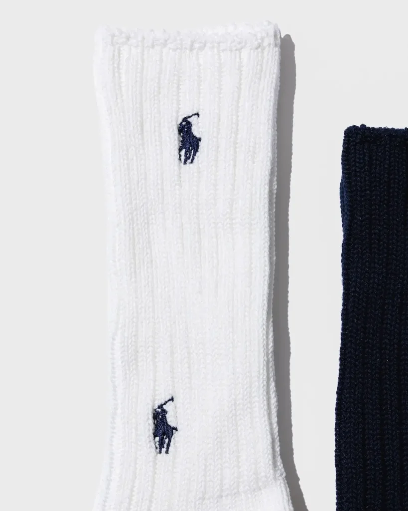 White ribbed sock with two navy polo-player logos beside a partially visible navy sock on a white background