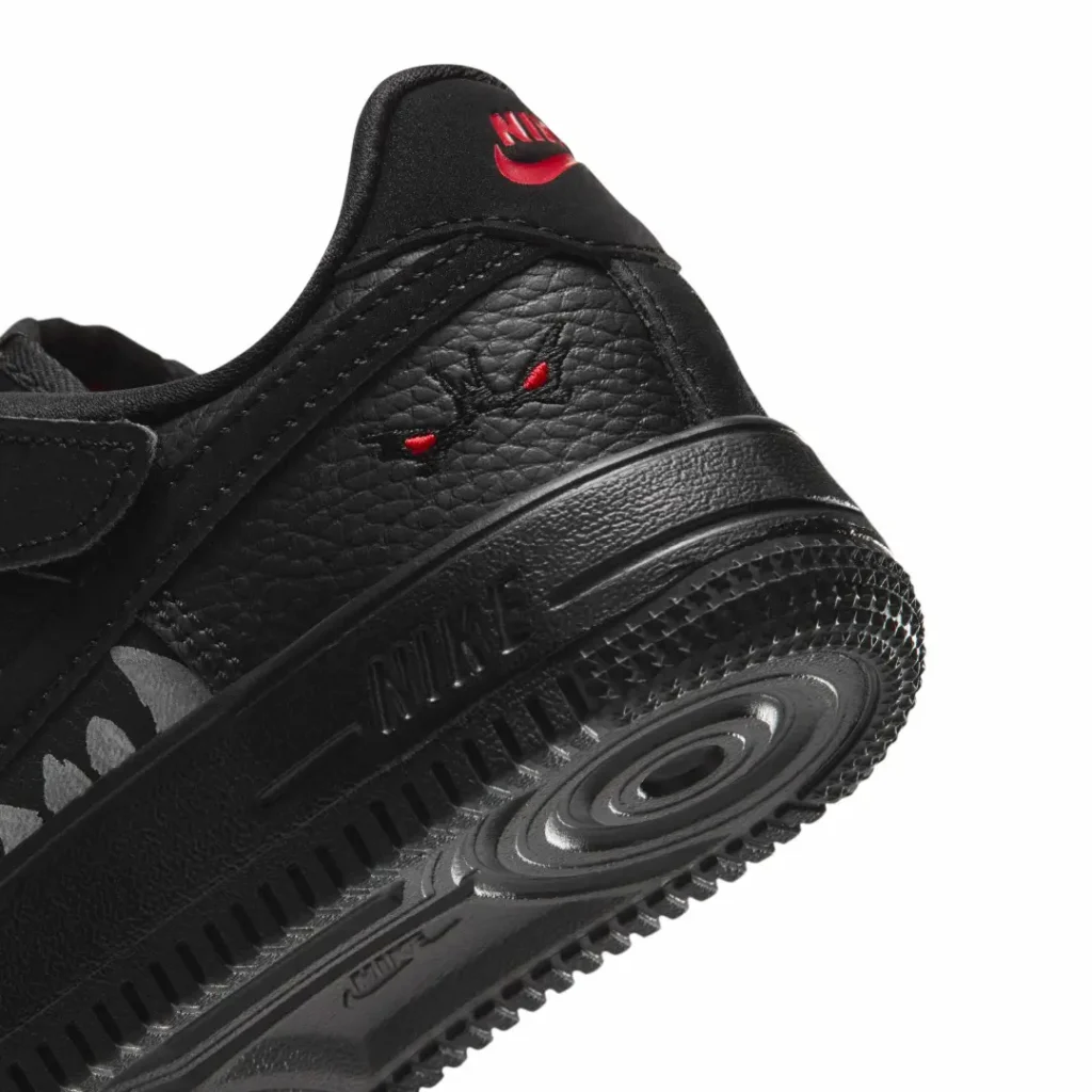 Close-up of a black leather shoe with red logo accent and a texture rubber sole against a white background