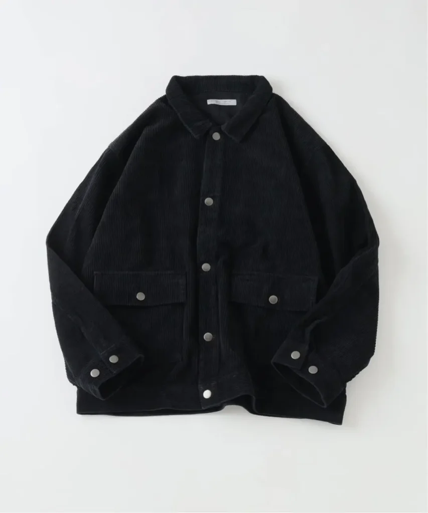 Black corduroy jacket with pointed collar, silver buttons, flap pockets and cuff tabs, laid flat on white background
