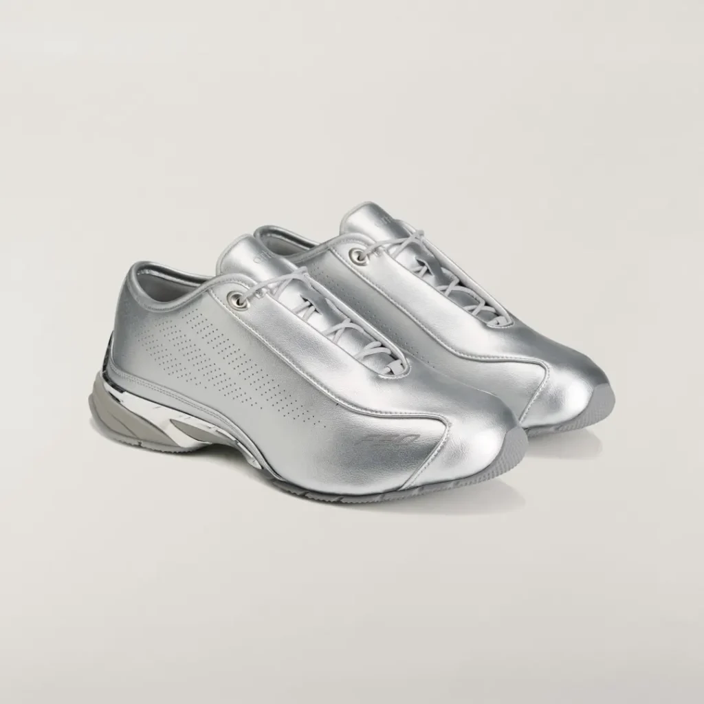 Pair of silver metallic low-top shoe with gray laces and perforated side panels on a light background