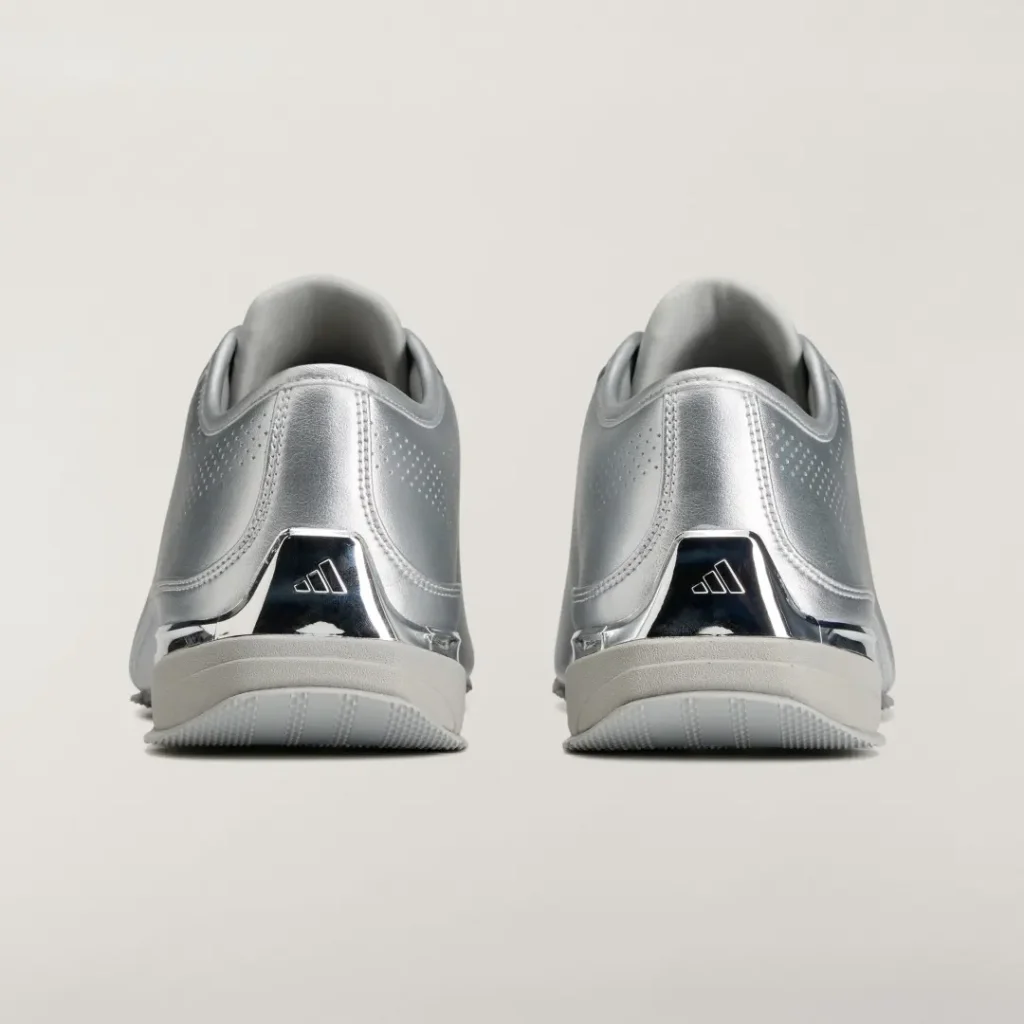 Rear view of matching silver Adidas shoe with reflective heel panels and white soles against a light background