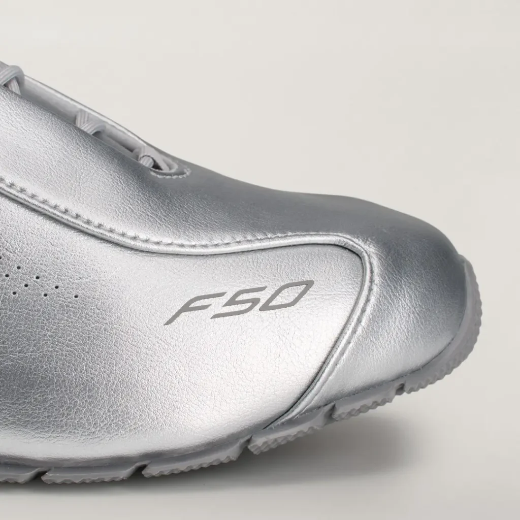 Close-up of a metallic silver F50 shoe showing stitched panels, perforations, logo, laces, and translucent rubber sole