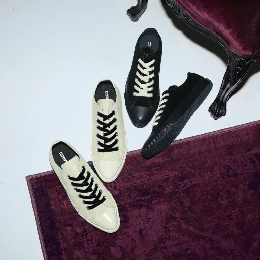 Four black and cream canvas sneakers arranged on a burgundy rug beside an ornate dark wood table-legged chair