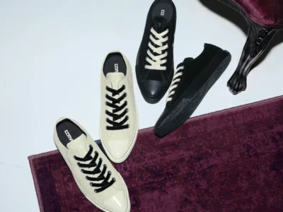 Four black and cream canvas sneakers arranged on a burgundy rug beside an ornate dark wood table-legged chair