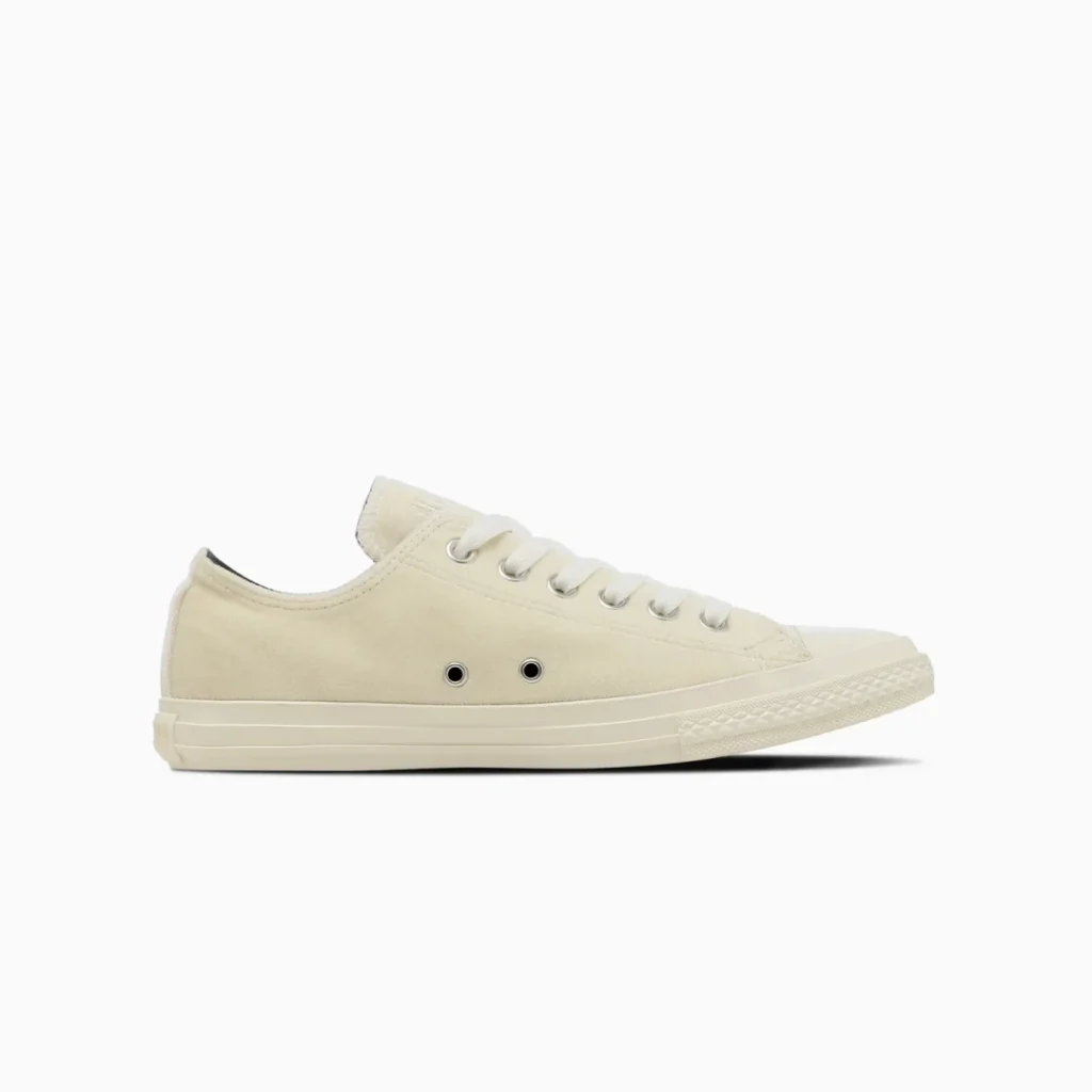 Cream canvas low-top sneaker with white laces, rubber toe cap, and side eyelets on a white background
