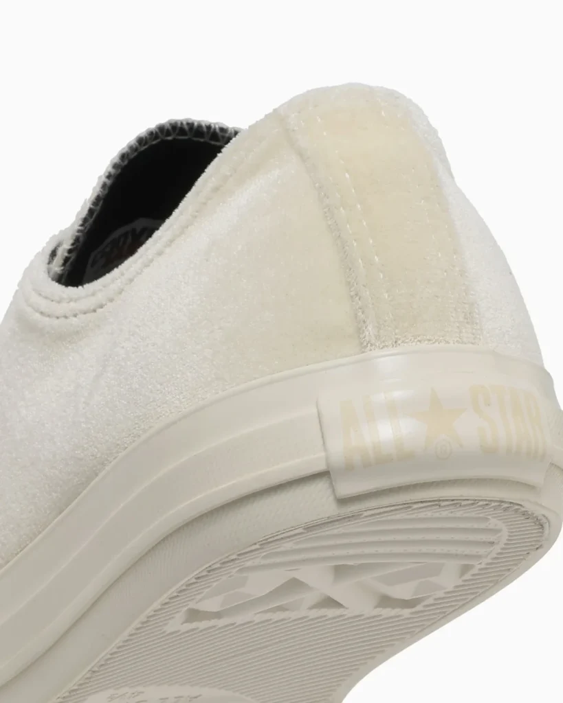Close-up of a white low-top sneaker showing textured fabric, rubber sole, and translucent heel patch with star logo