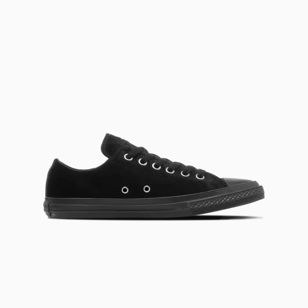 Black low-top canvas sneaker with black laces, silver eyelets, rubber toe cap and sole on a white background