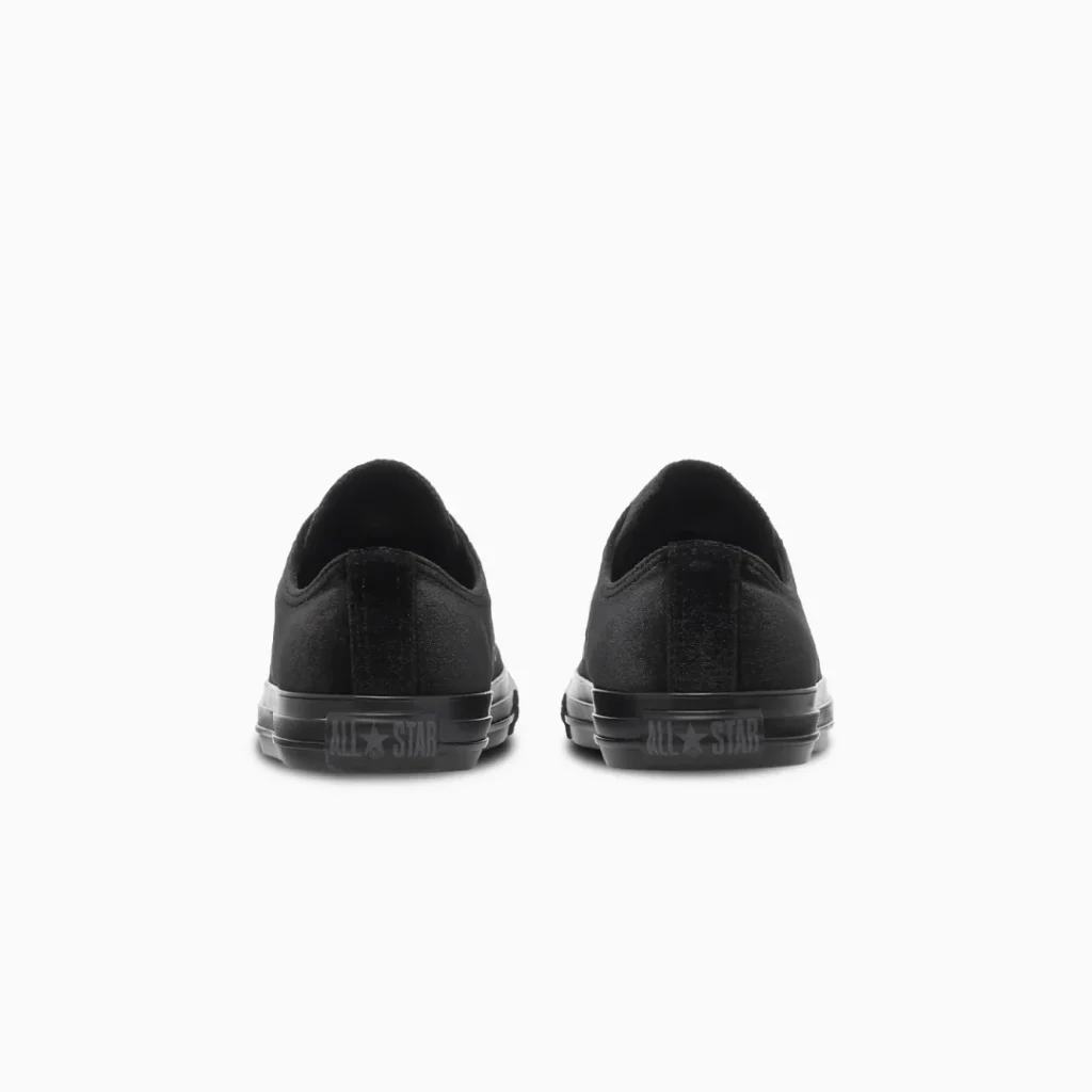 Rear view of a pair of black low-top sneakers with rubber soles and All Star branding on a white background