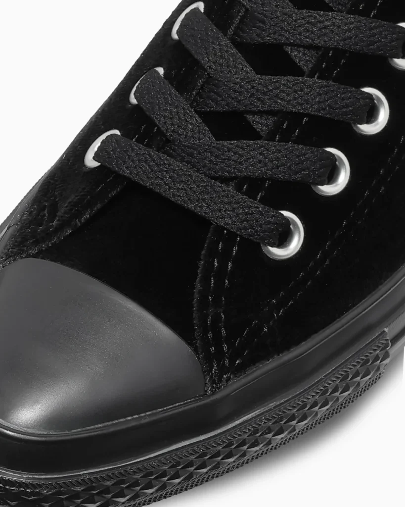 Close-up of a black sneaker with textured laces, silver eyelets and a patterned rubber sole against a white background