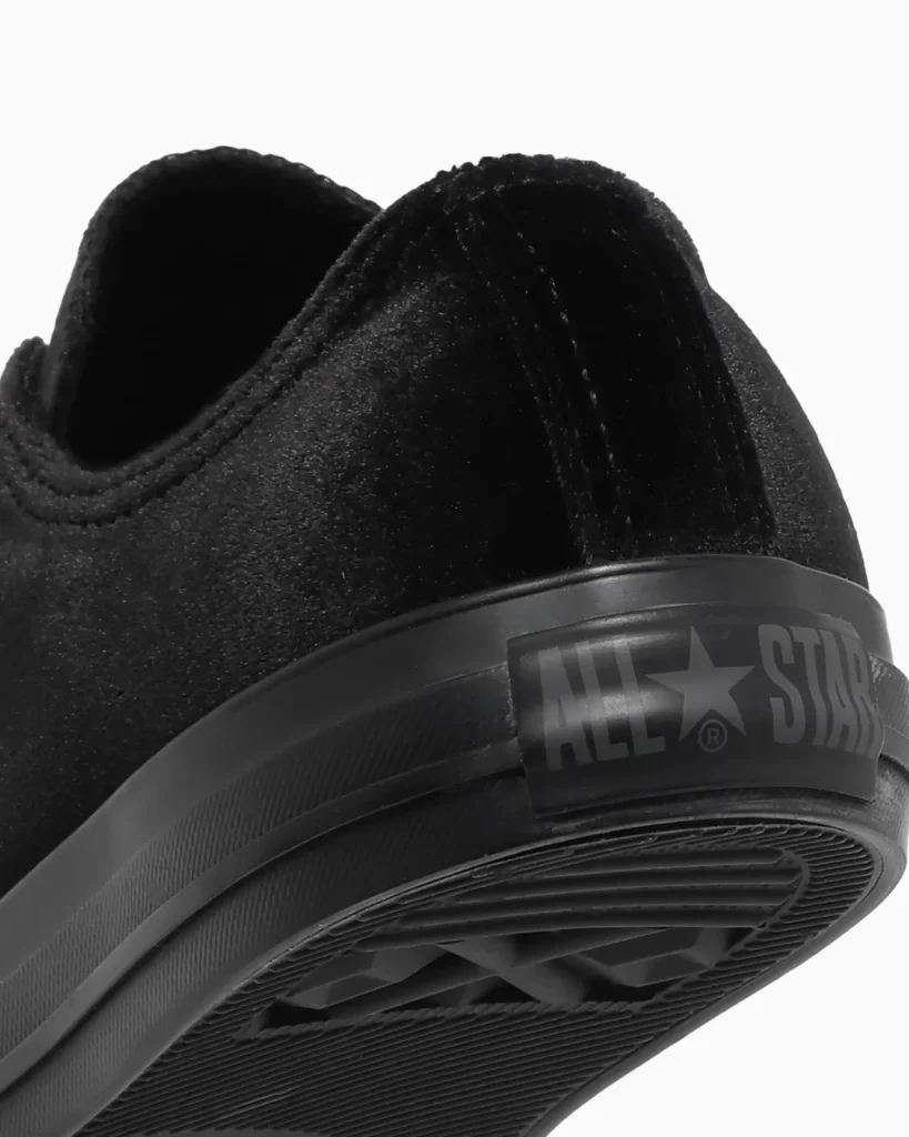 Close-up of a black Converse sneaker showing the textured upper, rubber sole, tread, and All Star ankle patch against white