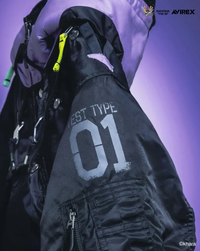 Close-up of a black MA-1 bomber jacket sleeve marked “TEST TYPE-01,” with utility pockets and neon yellow zipper pull