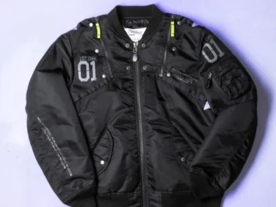 Black satin MA-1 bomber jacket laid flat, with neon yellow zipper accents, gray “01” patches and multiple pockets on a