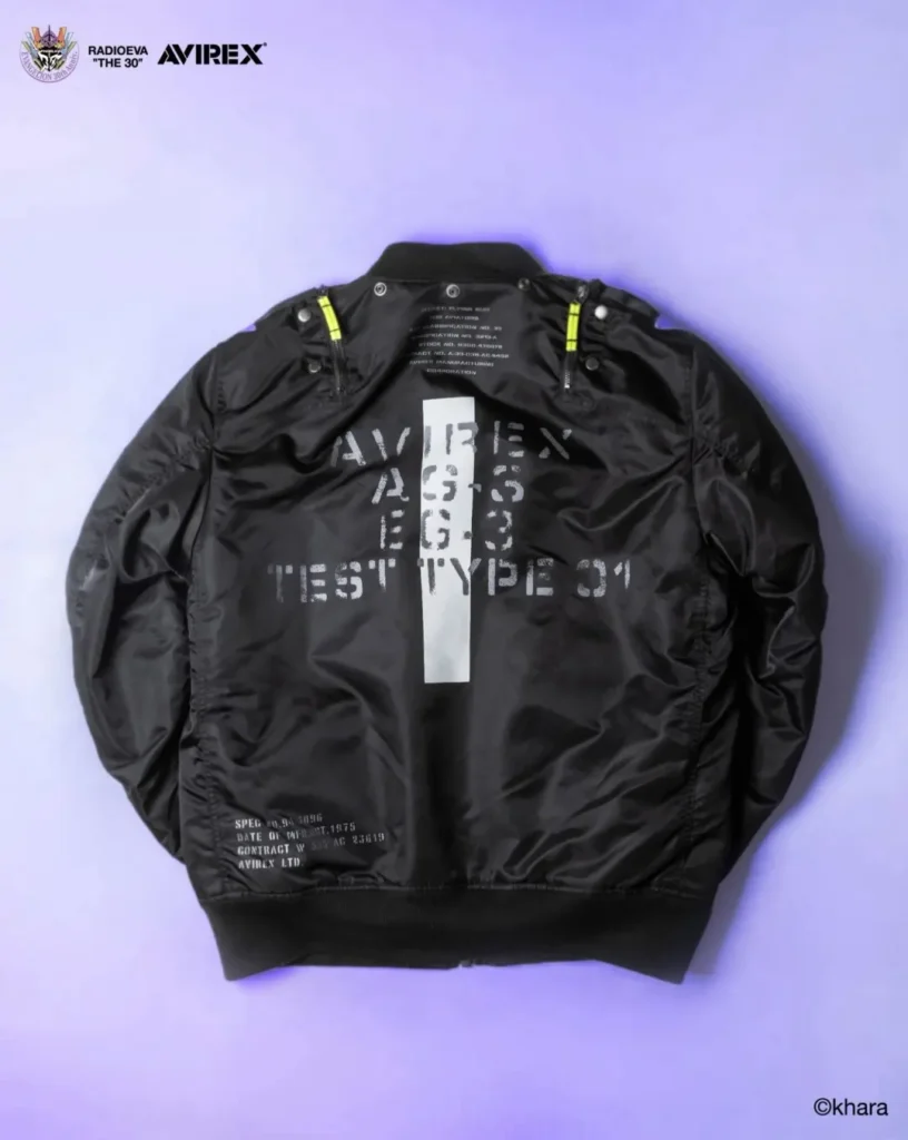 Black MA-1 bomber jacket laid flat on a lavender background, with white distressed lettering, a vertical white stripe, and